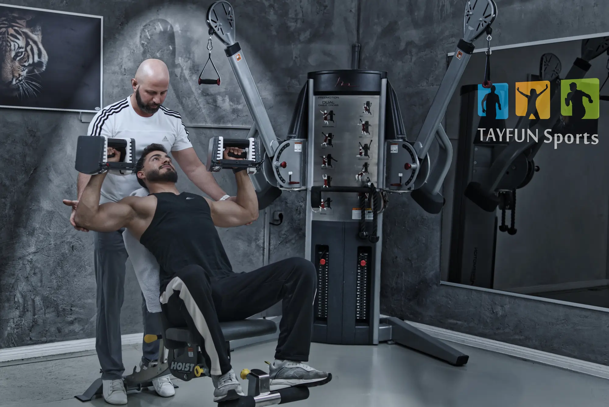 Trainer Tayfun beim Krafttraining mit einem Muskulösen Kunden.